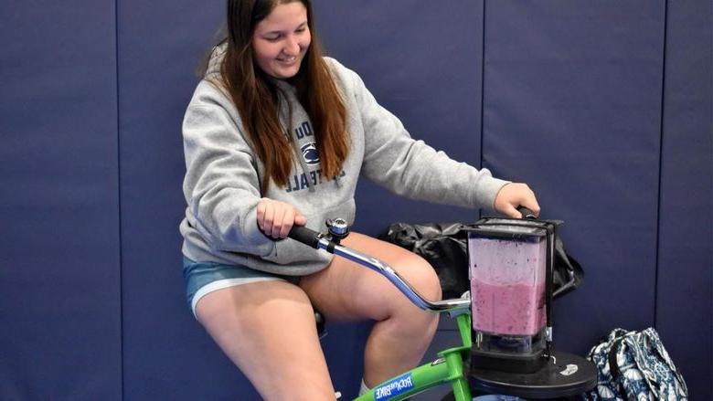 365英国上市杜波依斯分校 sophomore Aleigha Geer pedals the smoothie bike to make her smoothie during the Earth Day celebration at the PAW Center
